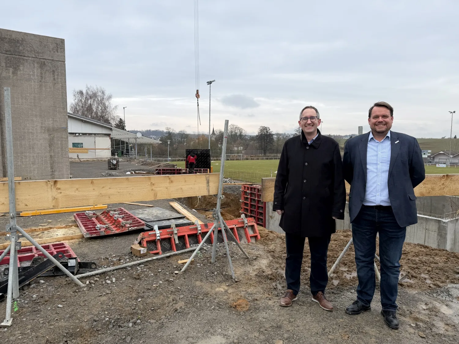 OB Sebastian Frei (l.) und Hochbauamtsleiter Alexander Speer auf der Baustelle der Krebsbachhalle in Obergimpern, im Hintergrund werden Verschaltungen für die neue Stützmauer gesetzt. (Bild: Stadt Bad Rappenau)
